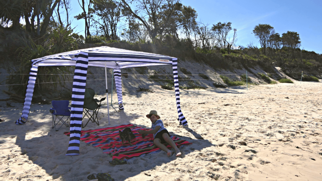 A boy laying underneath a CoolCabana beach shelter on the sand